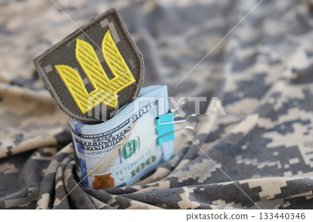 Ukrainian army symbol and bunch of dollar bills on military uniform. Payments to soldiers of the Ukrainian army from United States, salaries to the military. War support to Ukraine 133440346
