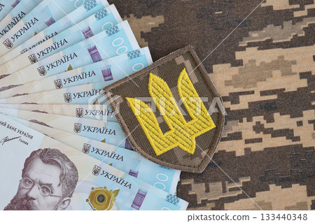 Ukrainian army symbol and bunch of hryvnia bills on military uniform. Payments to soldiers of the Ukrainian army, salaries to the military. War in Ukraine 133440348