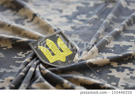 Symbol of Ukrainian army on the camouflage uniform of a Ukrainian soldier. The concept of war in Ukraine, patriotism and protecting your country from russian occupiers Symbol of Ukrainian army on the camouflage uniform of a Ukrainian soldier. The concept of war in Ukraine, patriotism and protecting your country from russian occupiers 133440350