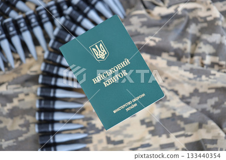 Ukrainian military ID on fabric with texture of pixeled camouflage. Cloth with camo pattern in grey, brown and green pixel shapes with Ukrainian army personal token and machine gun belt of bullets Ukrainian military ID on fabric with texture of pixeled camouflage. Cloth with camo pattern in grey, brown and green pixel shapes with Ukrainian army personal token and machine gun belt of bullets 133440354