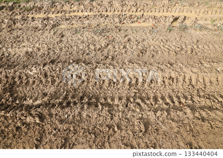 Wheel track on mud. Traces of a tractor or heavy off-road car on brown mud in a wet meadow Wheel track on mud. Traces of a tractor or heavy off-road car on brown mud in a wet meadow 133440404