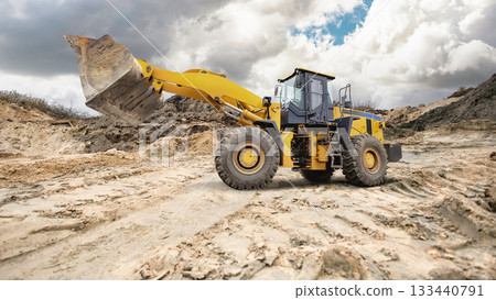 A large yellow loader moves dirt on a construction site under a dramatic sky. The surroundings show freshly disturbed earth and machinery in use A large yellow loader moves dirt on a construction site under a dramatic sky. The surroundings show freshly disturbed earth and machinery in use 133440791