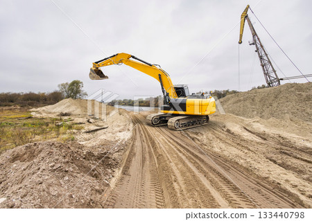 A powerful crawler excavator moves dirt along a riverside construction site under a cloudy sky, indicating progress in an ongoing development project A powerful crawler excavator moves dirt along a riverside construction site under a cloudy sky, indicating progress in an ongoing development project 133440798