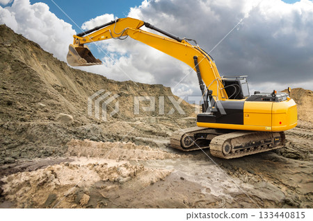 Heavy machinery digs into the earth at a construction site, moving dirt and debris while clouds gather above in the afternoon sky 133440815
