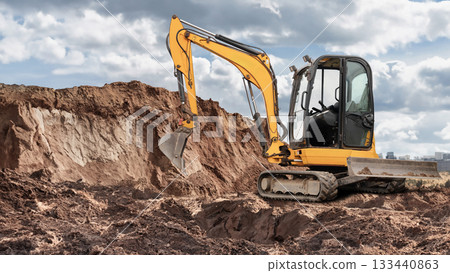An excavator digs into the earth at a construction site, moving dirt around while clouds gather overhead in an urban setting in the afternoon An excavator digs into the earth at a construction site, moving dirt around while clouds gather overhead in an urban setting in the afternoon 133440863
