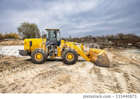 Construction equipment moves dirt at a site under a cloudy sky while preparing land for new development. Heavy machinery is actively engaged in work 133440873