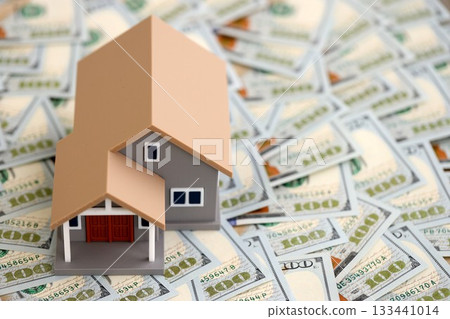 Toy house on big amount of US dollar bills close up. Real estate and building construction concept Toy house on big amount of US dollar bills close up. Real estate and building construction concept 133441014