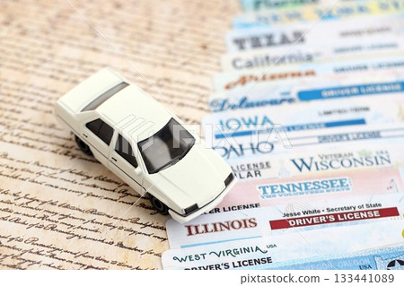 Toy car on big amount of driving licenses from different USA states on constitution page. Stack of driving license specimen cards Toy car on big amount of driving licenses from different USA states on constitution page. Stack of driving license specimen cards 133441089
