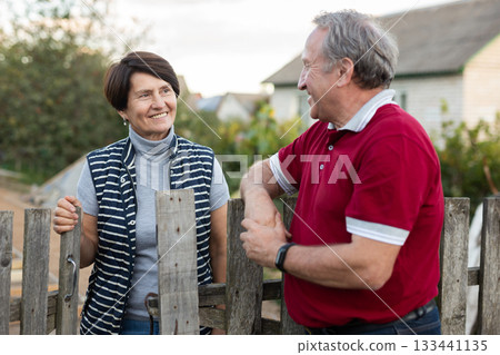 Two gardeners friendly talking outdoors next to wooden fence of country estate on day 133441135