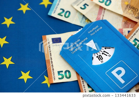 European parking disc with time dial on many euro money bills banknotes on flag of European Union. Concept of disc parking system in europe European parking disc with time dial on many euro money bills banknotes on flag of European Union. Concept of disc parking system in europe 133441633