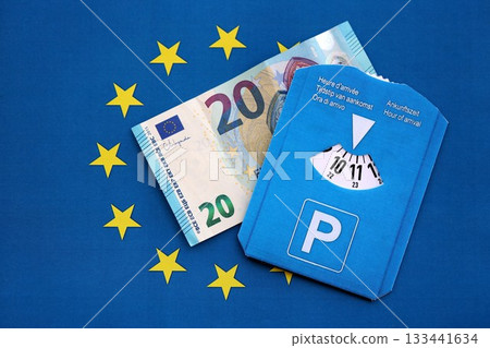 European parking disc with time dial and 20 euro money bill banknote on flag of European Union. Concept of disc parking system in europe European parking disc with time dial and 20 euro money bill banknote on flag of European Union. Concept of disc parking system in europe 133441634