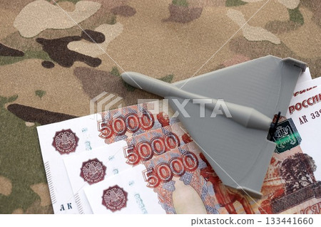 Russian money with bullets and kamikaze drone on multicam camouflage fabric close up. Concept of russian army funds and invasion to Ukraine Russian money with bullets and kamikaze drone on multicam camouflage fabric close up. Concept of russian army funds and invasion to Ukraine 133441660