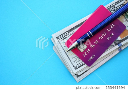 Credit card and pen with US dollar currency money bills banknotes on light blue background. Business, financial operations and accounting in United States of America Credit card and pen with US dollar currency money bills banknotes on light blue background. Business, financial operations and accounting in United States of America 133441694