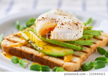 Breakfast with poached egg toast with avocado, vegetarian food.Healthy sandwich with avocado and poached eggs. Breakfast with poached egg toast with avocado, vegetarian food.Healthy sandwich with avocado and poached eggs. 133444421