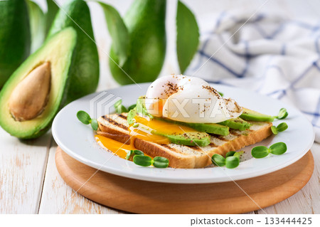 Breakfast with poached egg toast with avocado, vegetarian food.Healthy sandwich with avocado and poached eggs. Breakfast with poached egg toast with avocado, vegetarian food.Healthy sandwich with avocado and poached eggs. 133444425