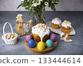 Easter kulich with candied fruits in white glaze with colorful sprinkles and painted eggs. Traditional Easter pastry. Easter holiday. Close-up, selective focus. 133444614