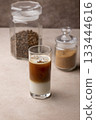 Coffee with coconut milk and ice cubes in a tall glass. Traditional non-alcoholic cold drink. In the background, a jar of coffee and a jar of sugar. Selective focus, close-up. 133444616