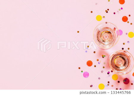 Two champagne glasses with sparkling wine on pink background, surrounded by colorful confetti, create festive and joyful atmosphere for celebration or party event 133445766