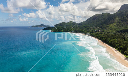 Clear turquoise waters meeting a secluded beach and dense forest surrounded by rocky formations. Grand Anse. Seychelles, Mahe. 133445910