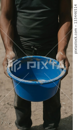 A man holds a blue bucket filled with a mixture of sand and cement 133446514