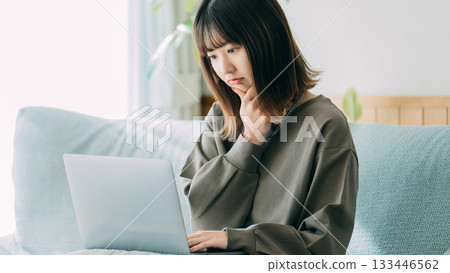一位女士在沙發上一邊使用電腦一邊思考。 133446562