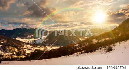 panorama of winter countryside in mountains at sunset. wonderful forest on the snow covered hills in evening light. village down in the distant valley. faraway ridge with snowy tops. timeless panorama of winter countryside in mountains at sunset. wonderful forest on the snow covered hills in evening light. village down in the distant valley. faraway ridge with snowy tops. timeless 133446704
