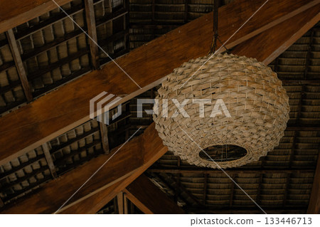 Woven rattan lamp against wooden beams creating a cozy yet eco-friendly atmosphere that supports sustainability 133446713
