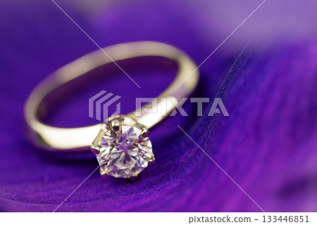 A gold and diamond ring is on a purple background 133446851