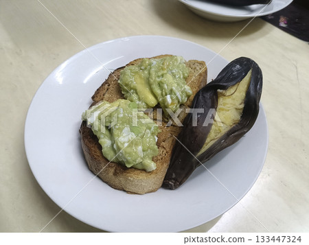 Avocado mash on toasted bread with roasted banana on plate, simple rustic breakfast with creamy texture 133447324