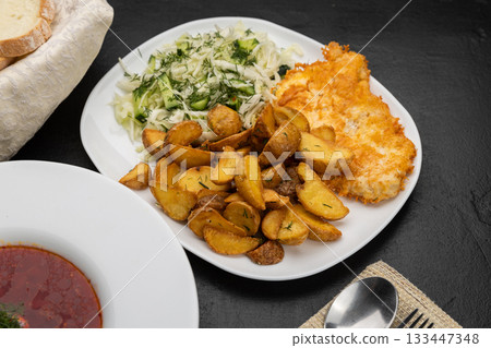 Closeup of fried potato wedges with chicken schnitzel and cabbage salad on white plate 133447348