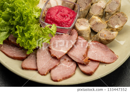 Charcuterie platter with pork slices, sausage, lettuce and red sauce on plate, closeup Charcuterie platter with pork slices, sausage, lettuce and red sauce on plate, closeup 133447352