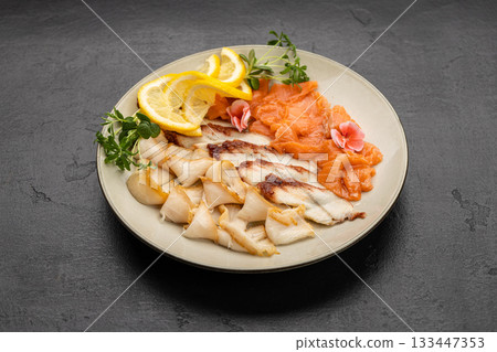Assorted smoked fish platter with salmon, lemon slices and microgreens on plate 133447353