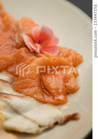 Close up of salmon sashimi with edible flower garnish on plate Close up of salmon sashimi with edible flower garnish on plate 133447358