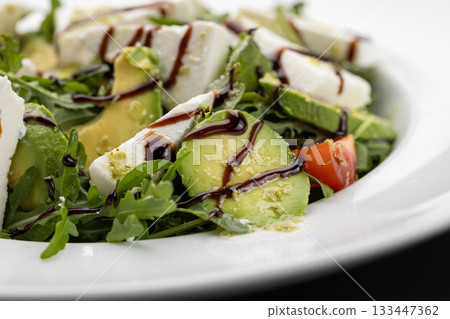 Close up of avocado arugula salad with feta and balsamic glaze on white plate 133447362