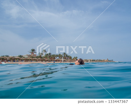 A young woman with sun glasses swimming in the blue sea. A blue hazy sky in the background A young woman with sun glasses swimming in the blue sea. A blue hazy sky in the background 133447367