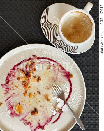 Finished dessert plate with cappuccino cup, pastry crumbs, berry syrup traces, suggesting cozy Thanksgiving treat just enjoyed. Concept of satisfying fall flavors and comforting moments Finished dessert plate with cappuccino cup, pastry crumbs, berry syrup traces, suggesting cozy Thanksgiving treat just enjoyed. Concept of satisfying fall flavors and comforting moments 133447615