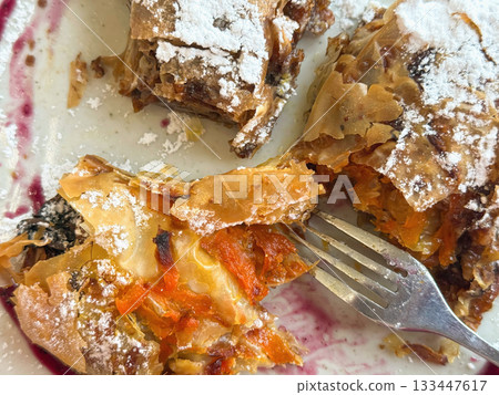 Close-up of sliced pumpkin strudel with visible orange vegetable filling and crispy filo crust, sprinkled with powdered sugar. Handmade Thanksgiving pastry rich in autumn flavors 133447617