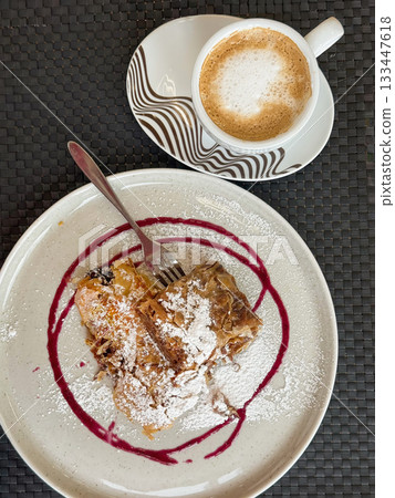Cup of cappuccino served with slice of pumpkin strudel on ceramic plate with powdered sugar and berry syrup. Thanksgiving dessert break with warm coffee and cozy seasonal flavors Cup of cappuccino served with slice of pumpkin strudel on ceramic plate with powdered sugar and berry syrup. Thanksgiving dessert break with warm coffee and cozy seasonal flavors 133447618