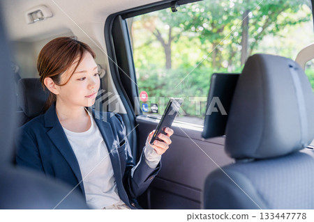 A young female business person using a smartphone in a taxi 133447778