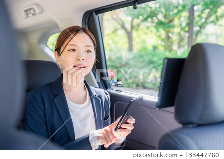 A young female business person using a smartphone in a taxi 133447780