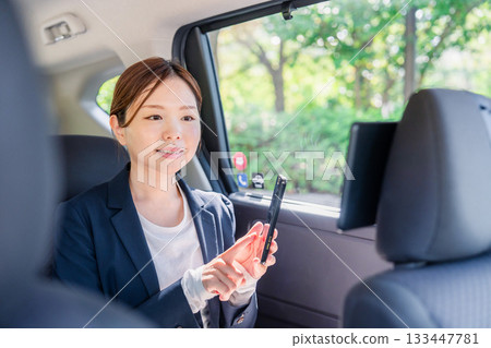 一位年輕的女商務人士在計程車裡使用智慧型手機。 133447781