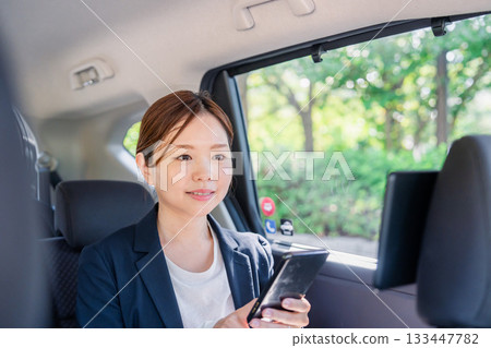 一位年輕的女商務人士在計程車裡使用智慧型手機。 133447782