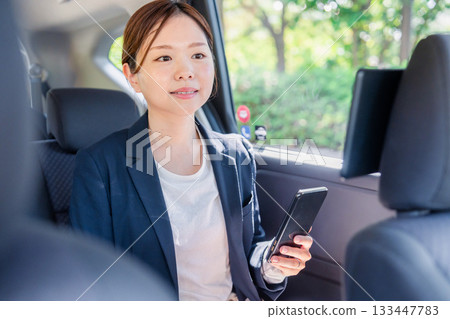 一位年輕的女商務人士在計程車裡使用智慧型手機。 一位年輕的女商務人士在計程車裡使用智慧型手機。 133447783