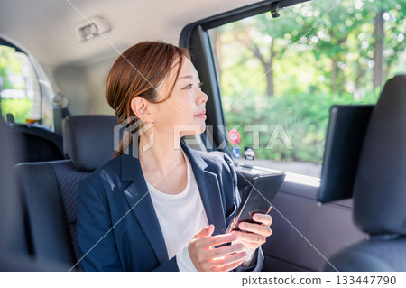 一位年輕的女商務人士在計程車裡使用智慧型手機。 133447790