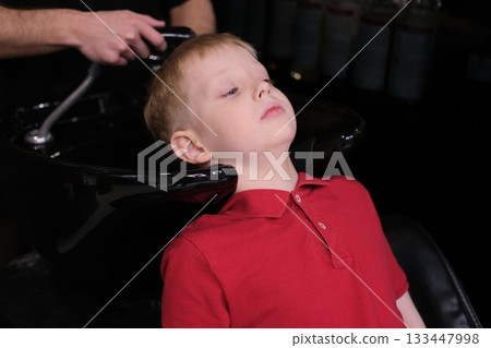 Young boy getting hair washed at barbershop sink 133447998