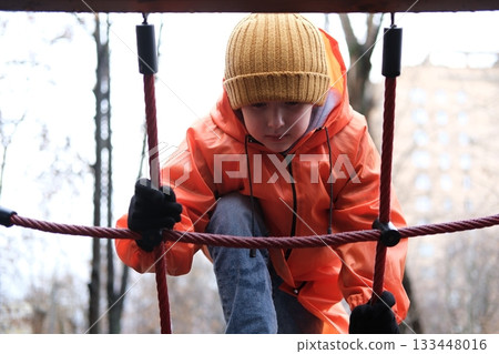 Child climbing rope net on playground in winter Child climbing rope net on playground in winter 133448016