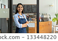 Indian woman entrepreneur smiling, standing with arms crossed in coffee shop. 133448220