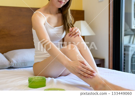 一位年輕苗條的女子穿著內衣,在床上塗抹身體凝膠,照顧雙腿。日間照顧。修剪整齊。 一位年輕苗條的女子穿著內衣,在床上塗抹身體凝膠,照顧雙腿。日間照顧。修剪整齊。 133449060