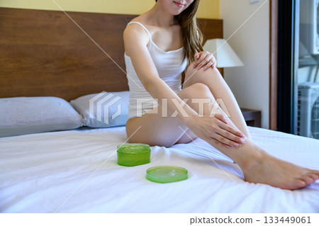 A young slender woman in underwear applying body gel to her legs in bed. Foot care. Morning color. A young slender woman in underwear applying body gel to her legs in bed. Foot care. Morning color. 133449061