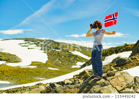 Tourist holds camera and norwegian flag in mountains Tourist holds camera and norwegian flag in mountains 133449242